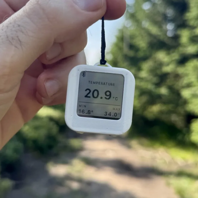 Thermio held in a hand on a forest trail, its display reading 20.9 °C