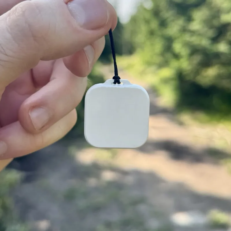 Thermio Mini held in a hand on a forest trail, showing its blank front with no display